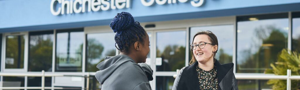 This is an image of two students outside the front of Chichester College laughing with each other.